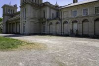 an old stone building that has grass on the outside and in front of it, next to a white fence and bushes