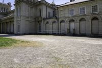 an old stone building that has grass on the outside and in front of it, next to a white fence and bushes