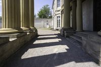 a pathway leading to some classical buildings with pillars and large round window frames with columns behind them