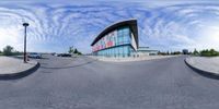 the view from the front and rear of a building while looking at a parking lot, with a cloudy blue sky behind it