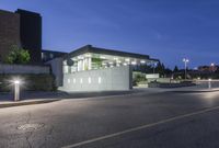 a concrete building at night with lights in front of it by a curb and sidewalk