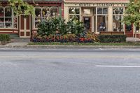 a store front in a small town surrounded by trees and flowers on a street corner