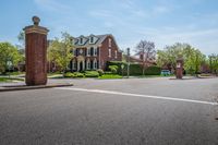 an open street in a neighborhood with two cars parked by the gate and large brick pillars