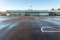 an empty parking lot in front of a building at the edge of a street with parking spaces in it