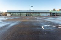 an empty parking lot in front of a building at the edge of a street with parking spaces in it