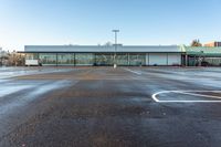 an empty parking lot in front of a building at the edge of a street with parking spaces in it