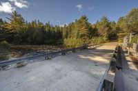 a view of an empty park with benches and bridge over water and trees to the side