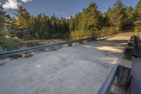 a view of an empty park with benches and bridge over water and trees to the side