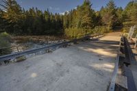 a view of an empty park with benches and bridge over water and trees to the side