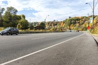 a car sits on the side of an empty road, overlooking city street and trees