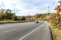 a car sits on the side of an empty road, overlooking city street and trees