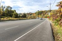 a car sits on the side of an empty road, overlooking city street and trees