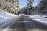 the empty road leads to a forest during the wintertime and snow covers it and there are trees lining the country side