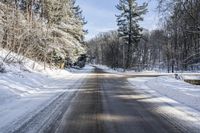 the empty road leads to a forest during the wintertime and snow covers it and there are trees lining the country side