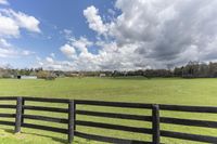 a field with a black wooden fence surrounded by clouds, and the sky is filled with clouds