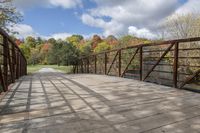 a wooden bridge over a paved path in the autumntime with fall foliage and a path winding through it