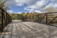 a wooden bridge over a paved path in the autumntime with fall foliage and a path winding through it