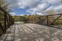 a wooden bridge over a paved path in the autumntime with fall foliage and a path winding through it