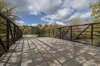 a wooden bridge over a paved path in the autumntime with fall foliage and a path winding through it