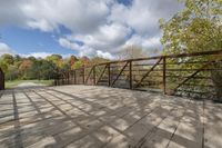 a wooden bridge over a paved path in the autumntime with fall foliage and a path winding through it