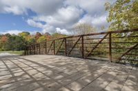 a wooden bridge over a paved path in the autumntime with fall foliage and a path winding through it