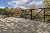 a wooden bridge over a paved path in the autumntime with fall foliage and a path winding through it