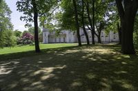 a large white house next to a field and trees in the yard with flowers on the grass