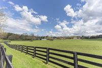 a fenced in area leading to a pasture with trees in the background and a barn in the distance