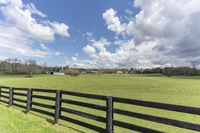 a fenced in area leading to a pasture with trees in the background and a barn in the distance