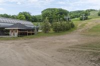 the dirt road is leading to a barn on a farm, which has a ski lift in the background