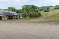 the dirt road is leading to a barn on a farm, which has a ski lift in the background