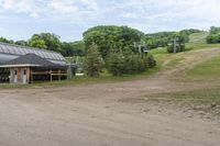 the dirt road is leading to a barn on a farm, which has a ski lift in the background