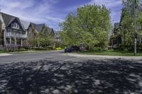 a residential neighborhood with lots of grass and tree, and two cars parked at the curb