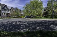 a residential neighborhood with lots of grass and tree, and two cars parked at the curb