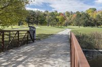 a wooden bridge over a paved path in the autumntime with fall foliage and a path winding through it