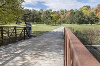 a wooden bridge over a paved path in the autumntime with fall foliage and a path winding through it