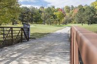 a wooden bridge over a paved path in the autumntime with fall foliage and a path winding through it