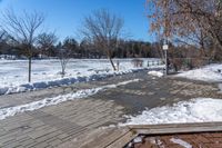 a walkway surrounded by snow next to a tree and bench in a park with clear skies