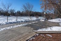 a walkway surrounded by snow next to a tree and bench in a park with clear skies