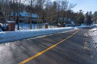 snow covered road going toward a large house on a sunny day next to trees and trees