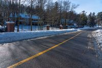 snow covered road going toward a large house on a sunny day next to trees and trees