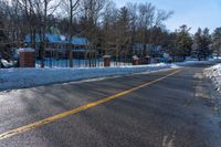 snow covered road going toward a large house on a sunny day next to trees and trees