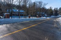 snow covered road going toward a large house on a sunny day next to trees and trees