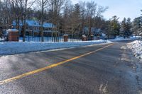 snow covered road going toward a large house on a sunny day next to trees and trees