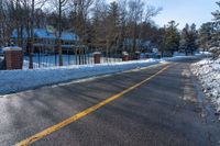 snow covered road going toward a large house on a sunny day next to trees and trees