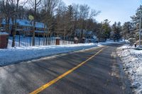 snow covered road going toward a large house on a sunny day next to trees and trees