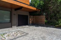 a home entrance, with stones surrounding, is surrounded by shrubbery and a wooden privacy fence