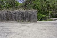 a wooden fence with sticks and plants growing on it in a parking lot next to trees