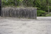 a wooden fence with sticks and plants growing on it in a parking lot next to trees