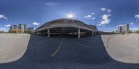 an empty parking lot under a cloudy blue sky with the sun peeking down, taken from below